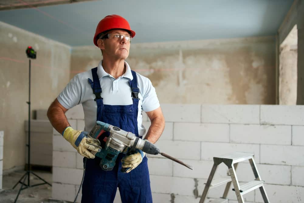 Professional Construction Worker In Uniform Standing With Rotary Hammer Drill.